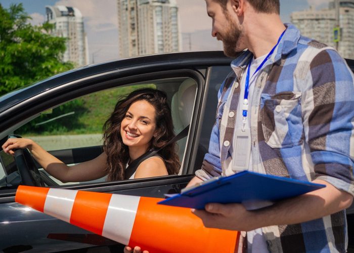 Male Instructor Holding Traffic Cone And Form. Young Woman Sitting In The Car Before Driving Lesson. Driving Test, Driver Courses, Exam Concept